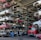 Numerous stacked rows of disassembled cars are placed on metal structures in what appears to be a scrapyard. Many of the cars are missing parts like wheels and doors.